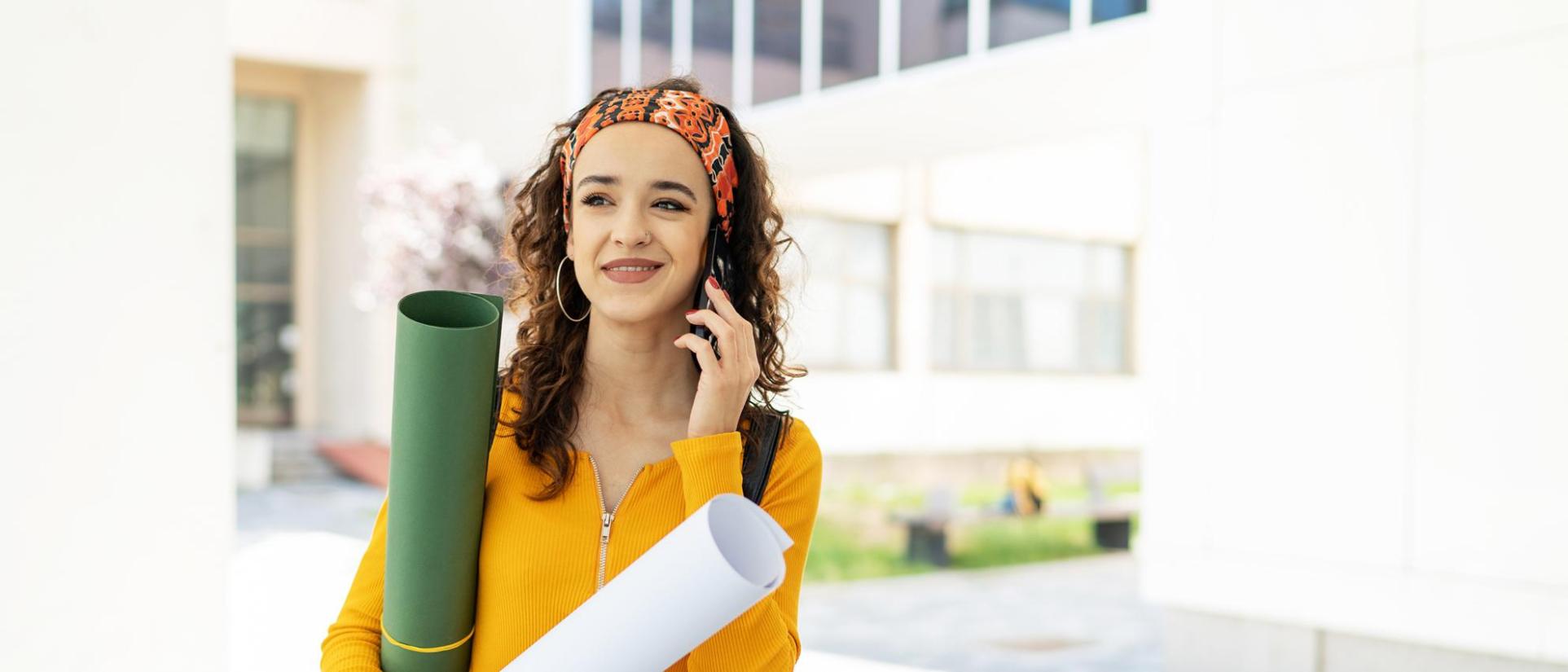 Beautiful, smiling, young woman holding cell phone to her ear, holding rolls of paper.