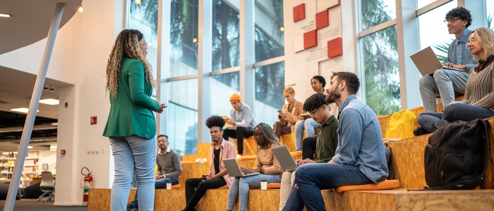 Woman in green blazer stands in front of group of seated young adult students looking up at her.