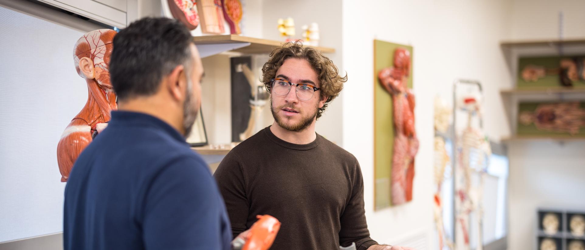 Men having a discussion, holding and surrounded by plastic models of human body parts and anatomy.