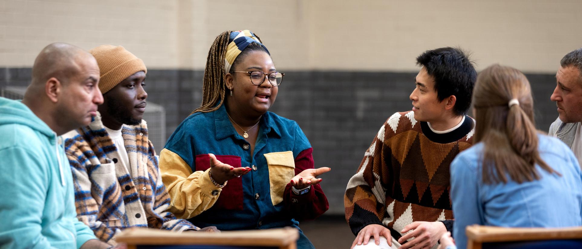 Woman sitting with 3 diverse men and one woman in a discussion circle.