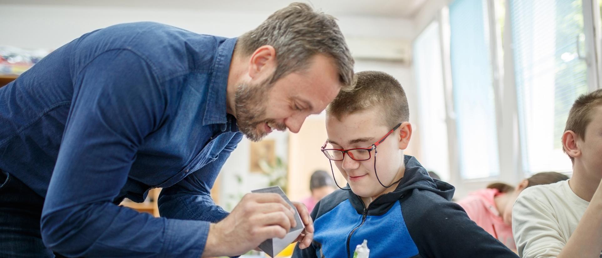 Teacher man with young special education student wearing red glasses.