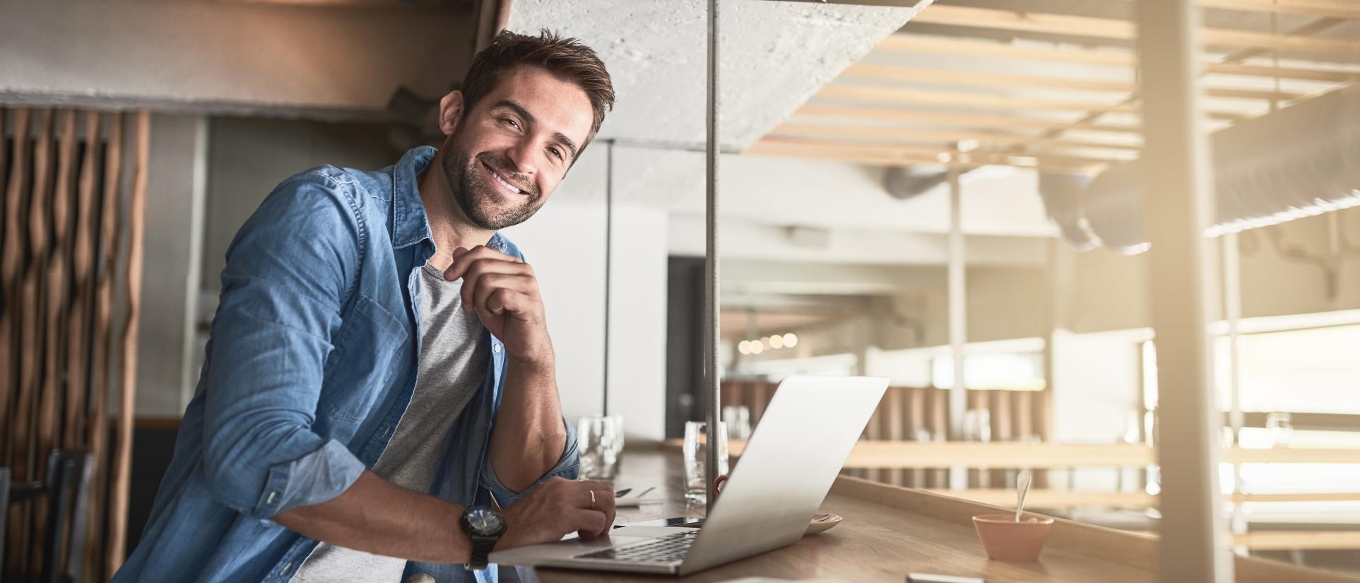 Man sits in front of a laptop, smiling.