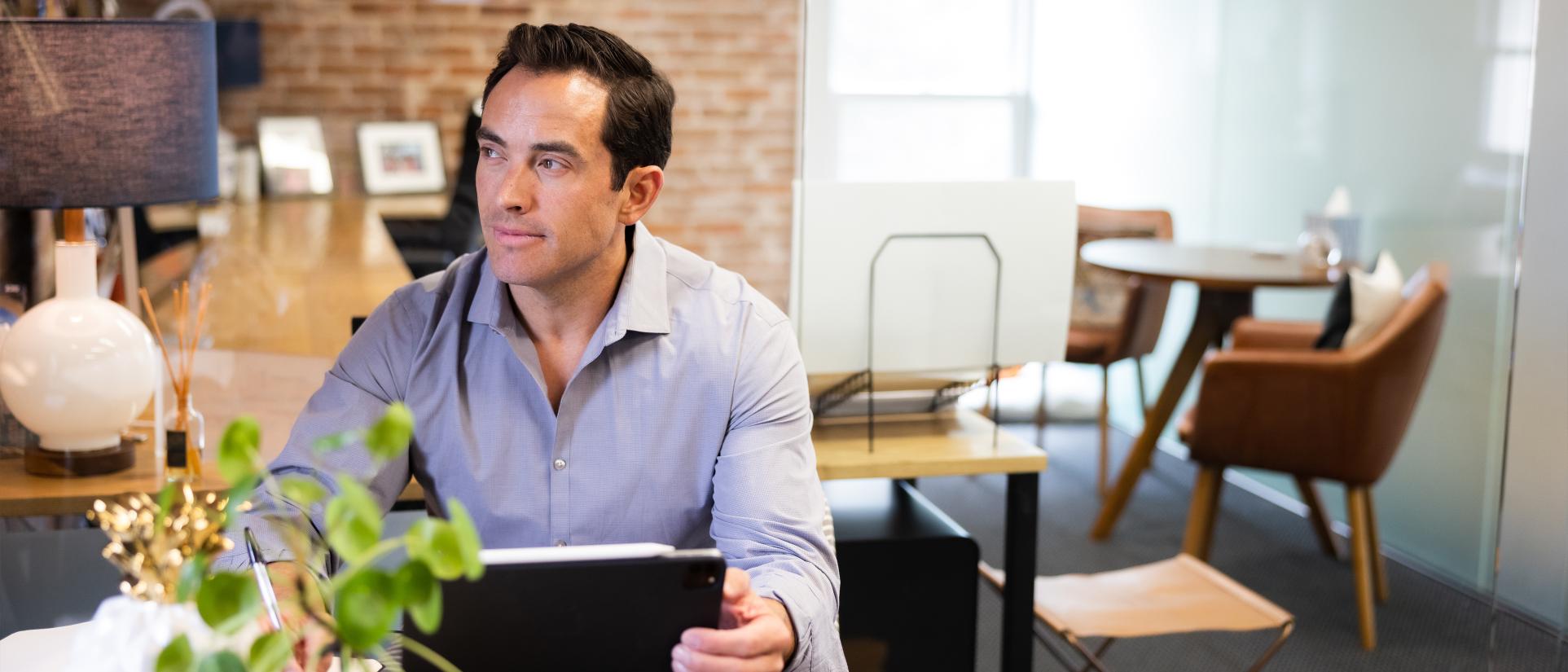Man sitting at desk, looks off into the distance with brick wall behind.