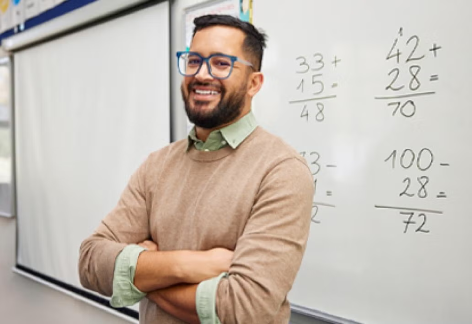 Smiling man in glasses folding his arms in front of white board with math.