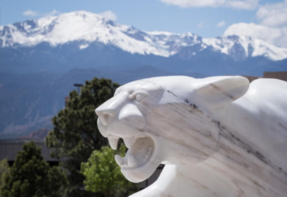 White marble statue of a mountain lion with snowy mountain range in the distant background.