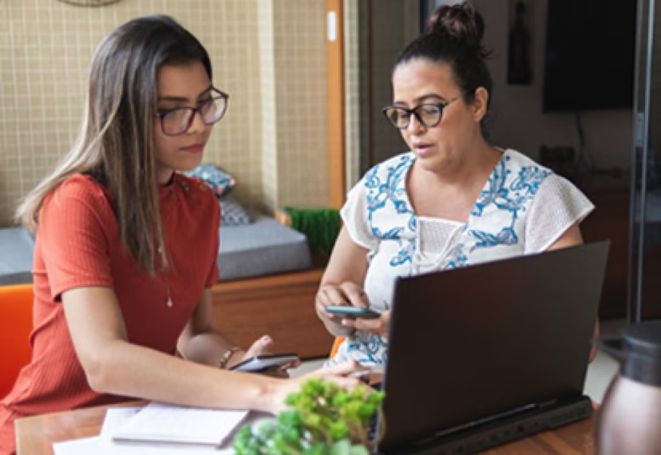 Hispanic mother and daughter holding calculators, paperwork, looking into laptop. 
