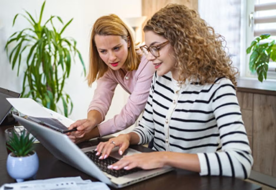 Mother and daughter looking into laptop with paperwork.