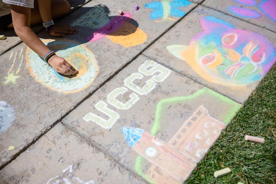 Sidewalk chalk art of UCCS, clocktower building and a hand in the frame drawing.