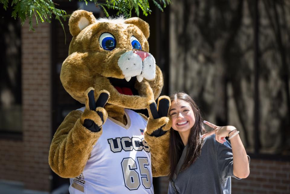 Young student with Clyde the mascot, both giving 2-finger peace sign hands.