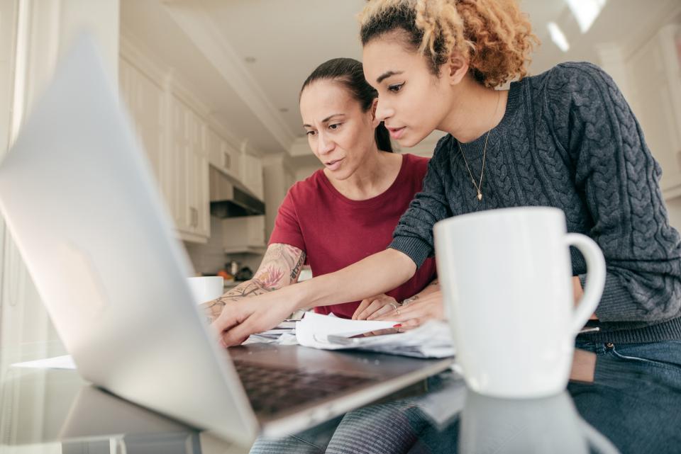 Younger and older women examining paperwork in front of laptop and coffee cup.