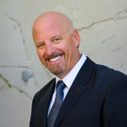 James H, Alum bald man with goatee, smiling in dark blue suit and tie.