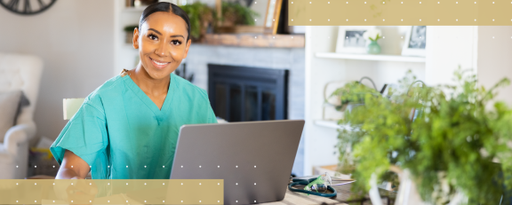 Young woman wearing nursing scrubs smiling and sitting at table in her living room with her laptop