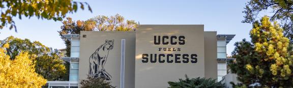 Clyde the Mountain Lion mascot image along with "UCCS Fuels Success" printed on a campus building.