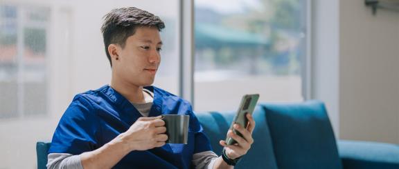A man in blue scrubs is reading on a mobile device. 