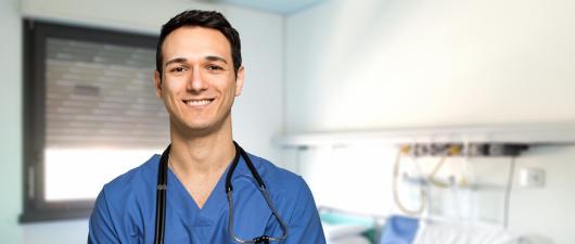 Male nurse smiling in blue scrubs with stethoscope around his neck.