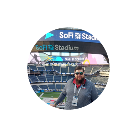 Man wearing sunglasses standing in front of the inside of the empty stands of a sporting arena, "SoFi" branded Stadium