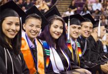 Multiple smiling UCCS graduates in regalia at graduation.