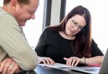 Middle-aged man and woman looking at paperwork and laptop.